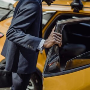 A businessman in a suit opens the door to a yellow taxi on a city street during the day.